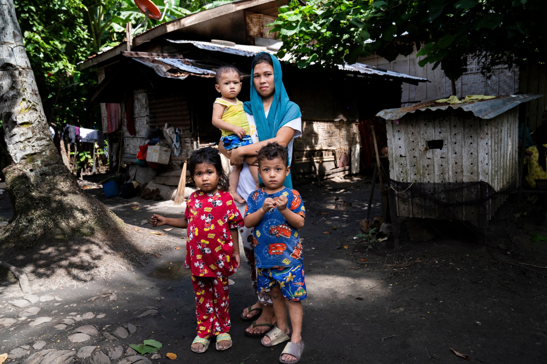 The Baraguir family — a mother holding a toddler with two young children standing in front of their home in the Philippines.