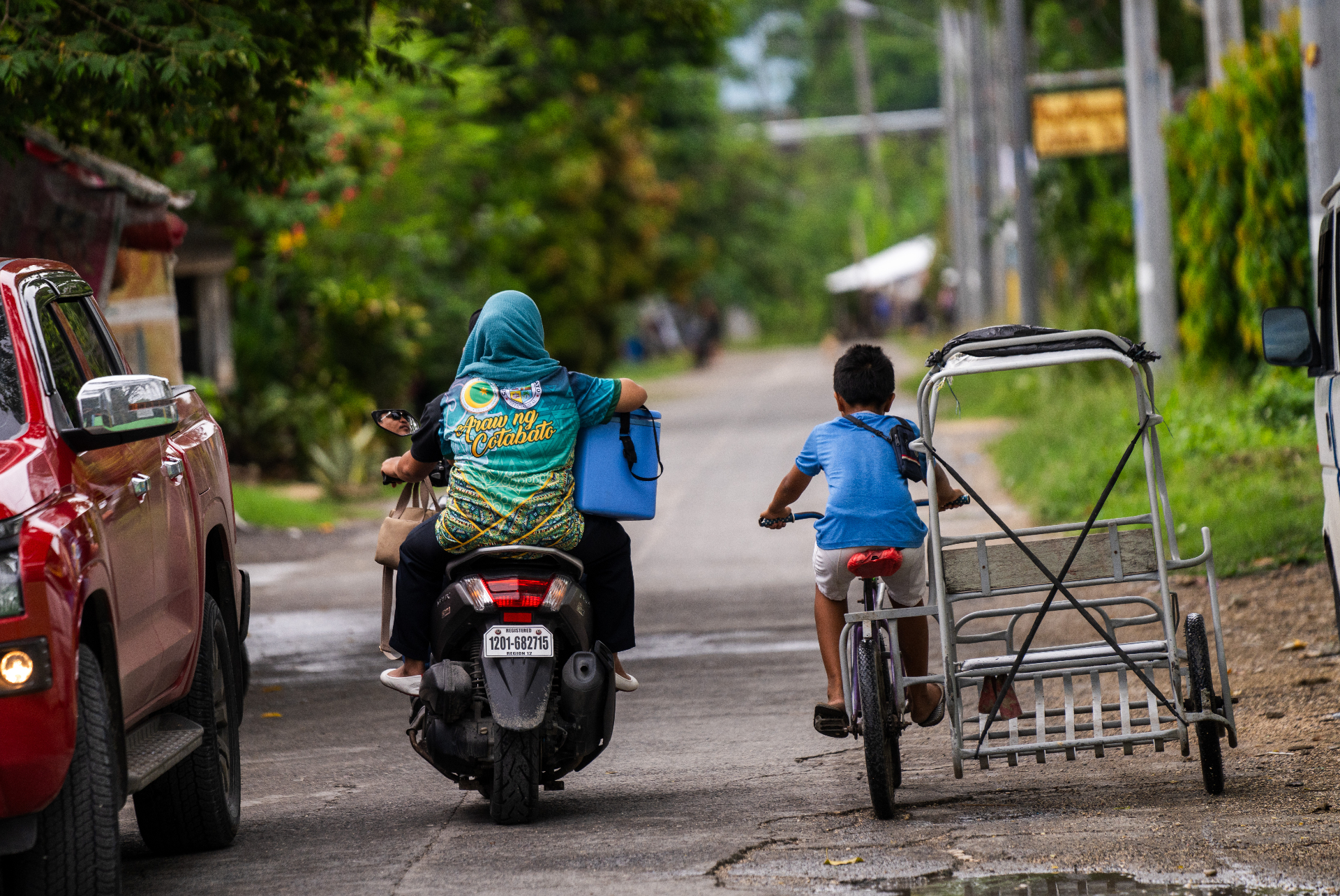 Midwife Tarhata Pangilan travels by motorbike carrying a vaccine cold box through a neighborhood in Cotabato City, Philippines, as a boy rides a bicycle alongside.